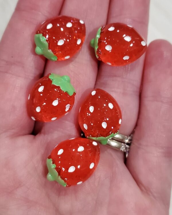 A hand holding four strawberries with white dots on them.