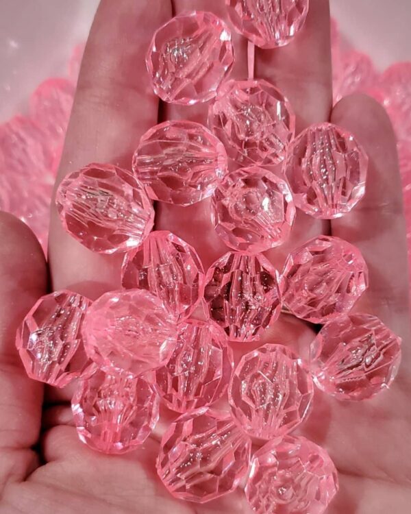 A hand holding pink beads in front of the camera.