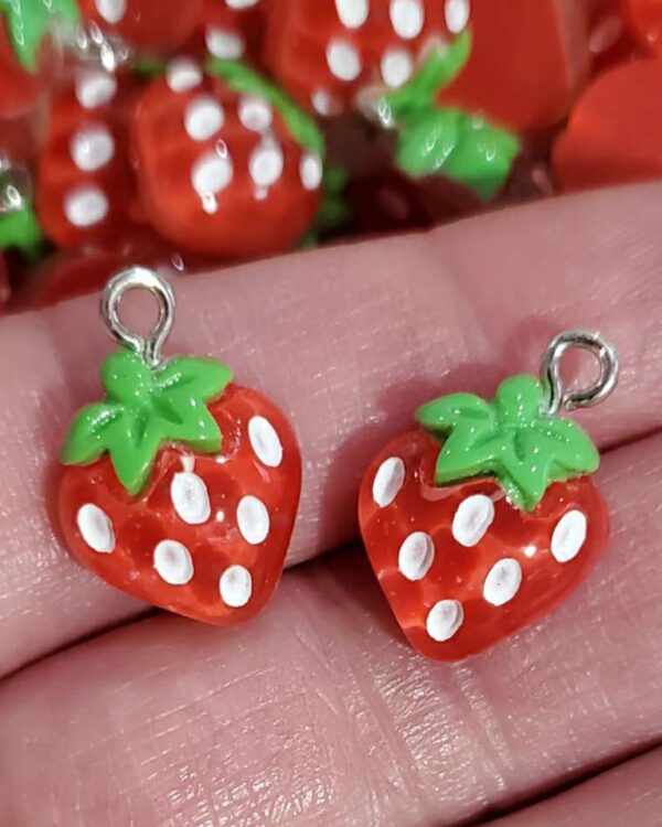 A hand holding up two strawberry charms.