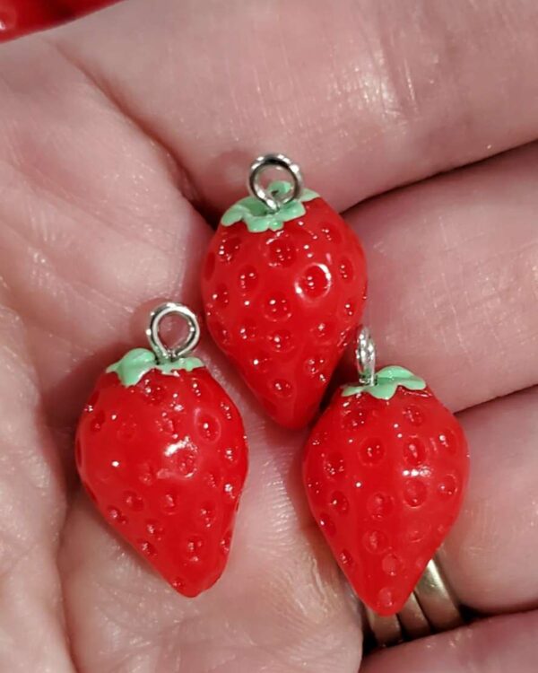 A hand holding three small red strawberries.